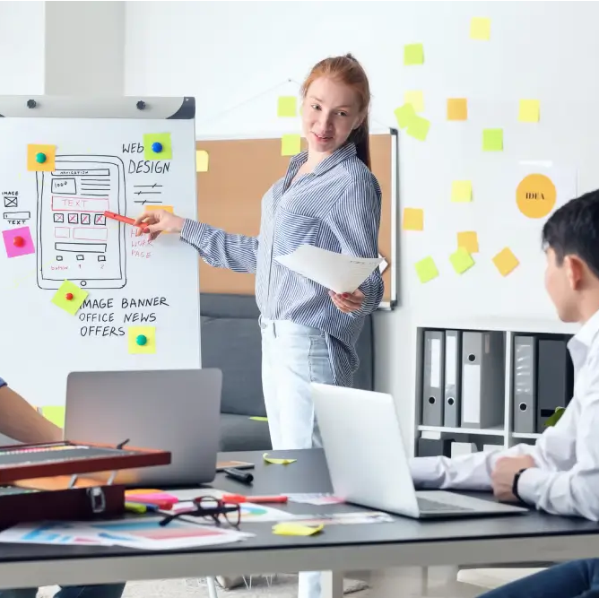 Woman presenting a website layout on a whiteboard to two colleagues in a modern office, discussing web design strategies and user experience.